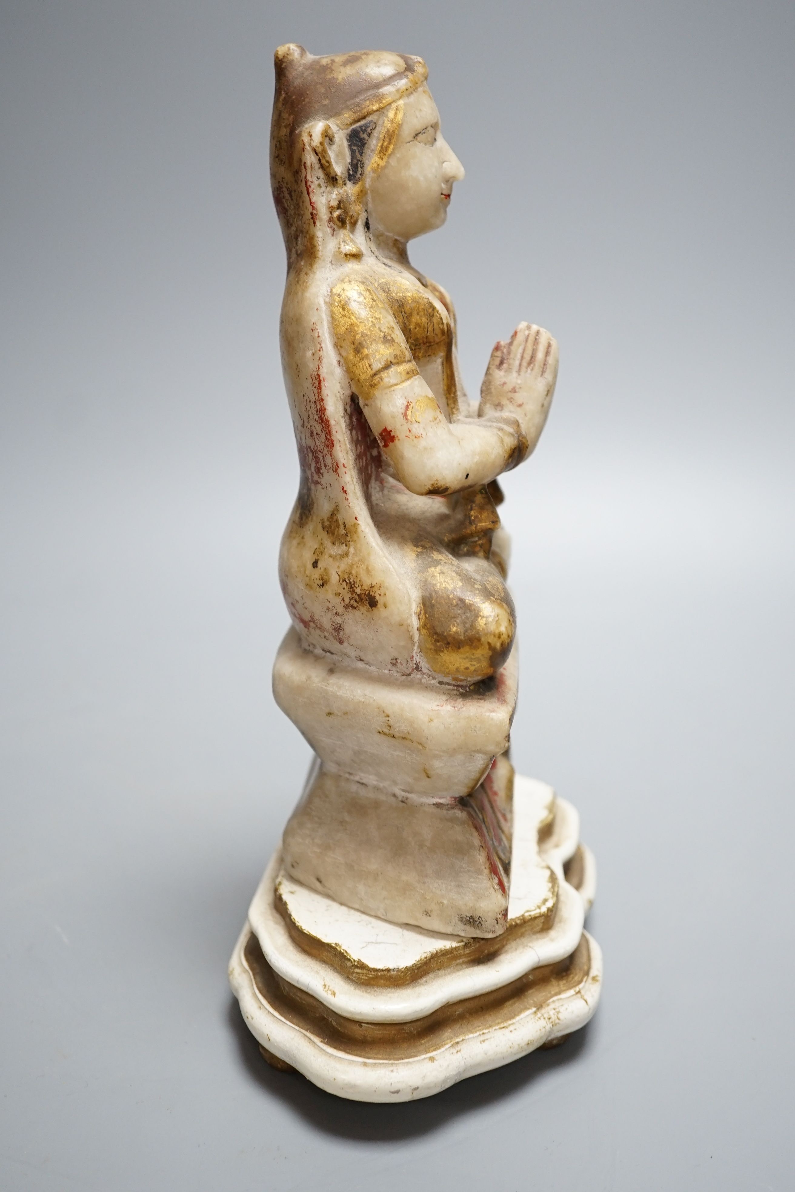 A late 19th century Indian carved alabaster seated figure, on associated wooden stand, 26cm